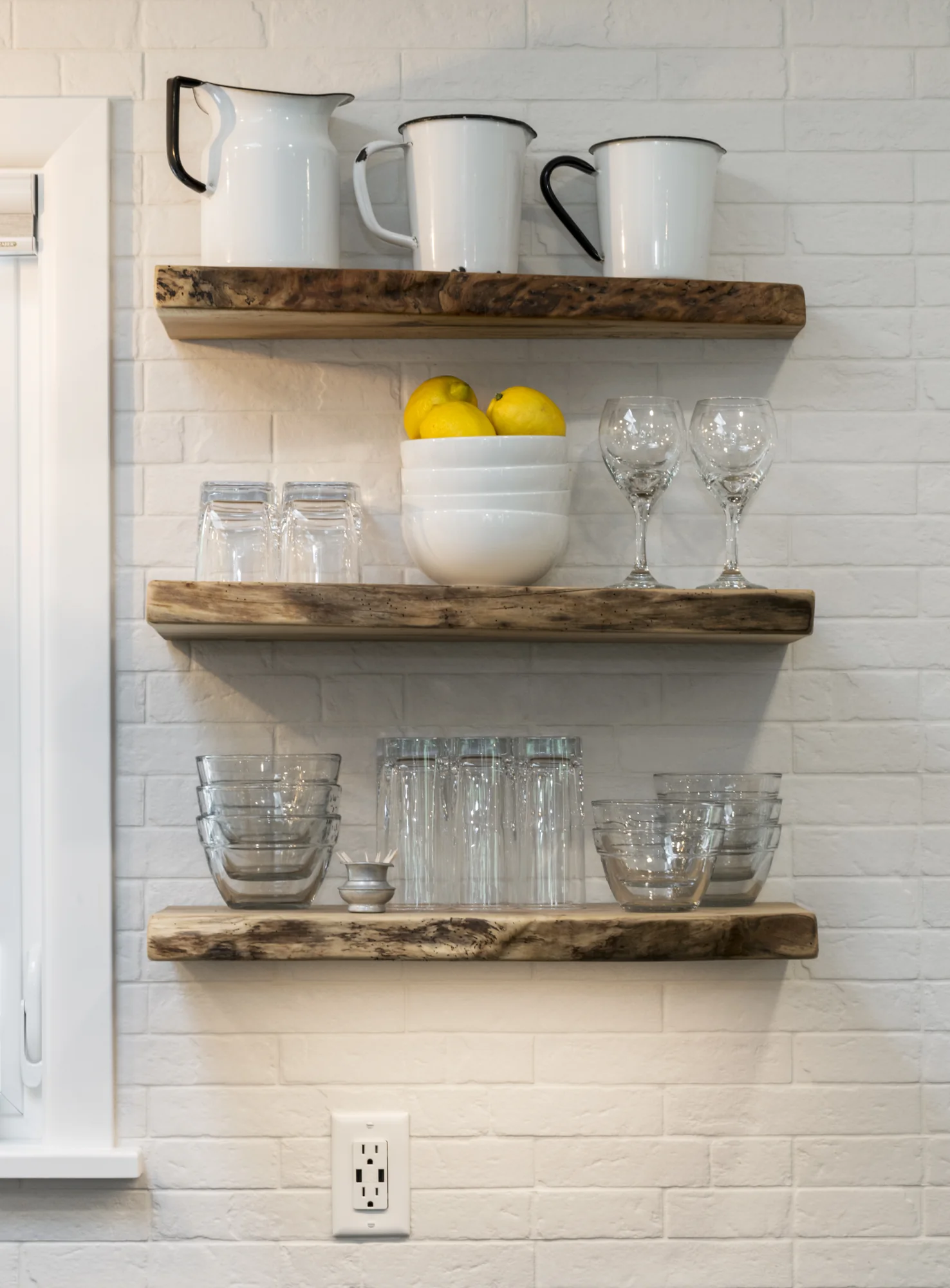 Natural wood open shelving on a white brick-pattern backsplash